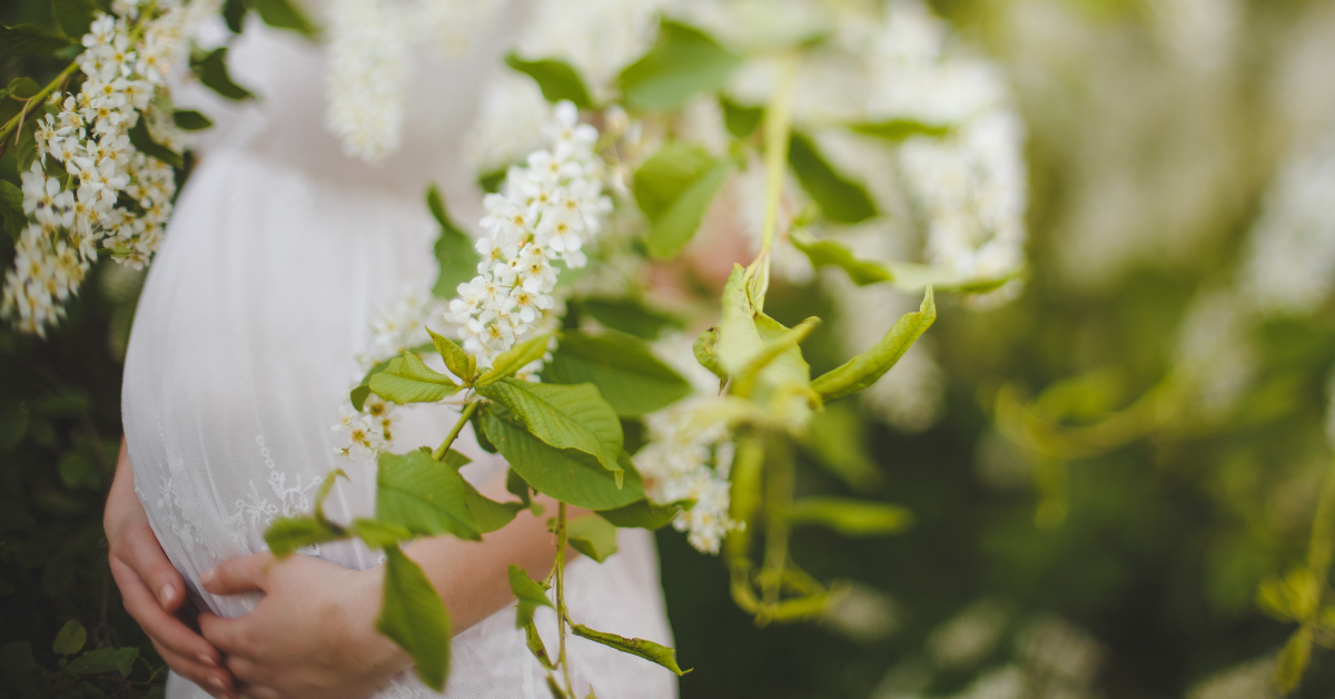 schwangere Frau in weißem Kleid hinter Ästen